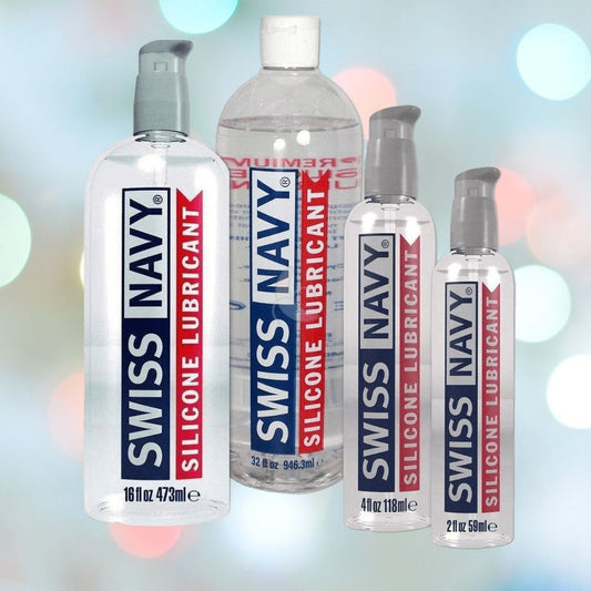 Displayed against a blurred background are four bottles of the Swiss Navy Silicone Lubricant, renowned for its enduring glide. These lubricants, characterized by their distinctive red and blue labels, offer a silky experience every time and come in sizes ranging from 2 oz to 32 oz. 1080