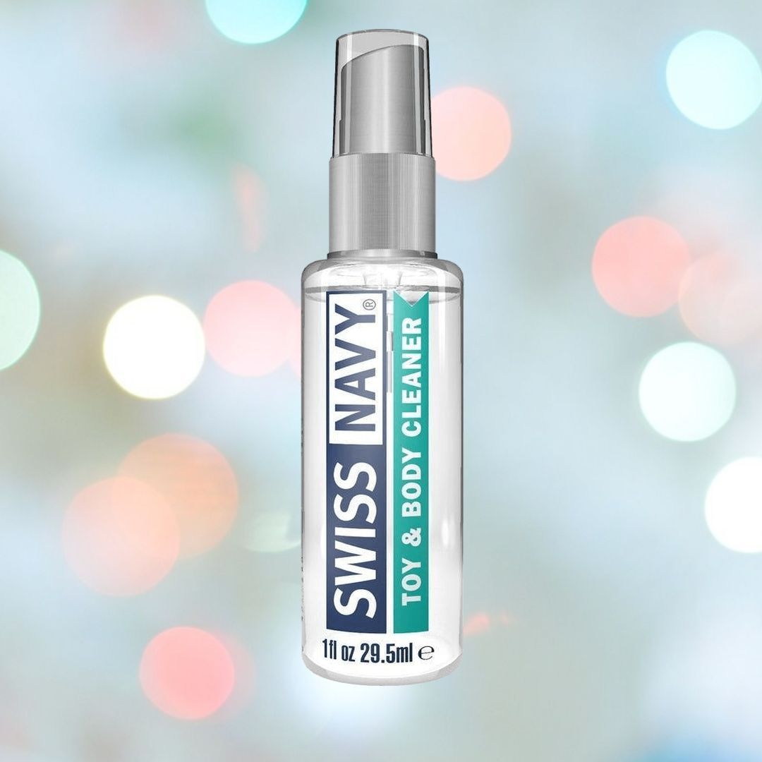 A clear bottle of Swiss Navy Toy and Body Cleaner, featuring information about its silicone lubricant-friendly formula, is positioned against a colorful, softly blurred background.