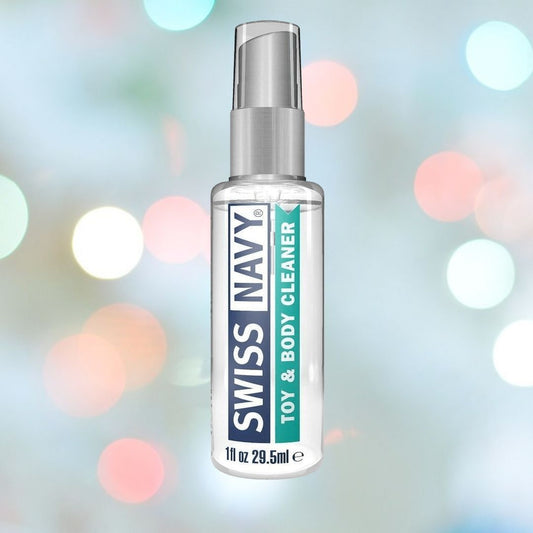 A clear bottle of Swiss Navy Toy and Body Cleaner, featuring information about its silicone lubricant-friendly formula, is positioned against a colorful, softly blurred background. 1080