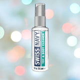 A clear bottle of Swiss Navy Toy and Body Cleaner, featuring information about its silicone lubricant-friendly formula, is positioned against a colorful, softly blurred background.