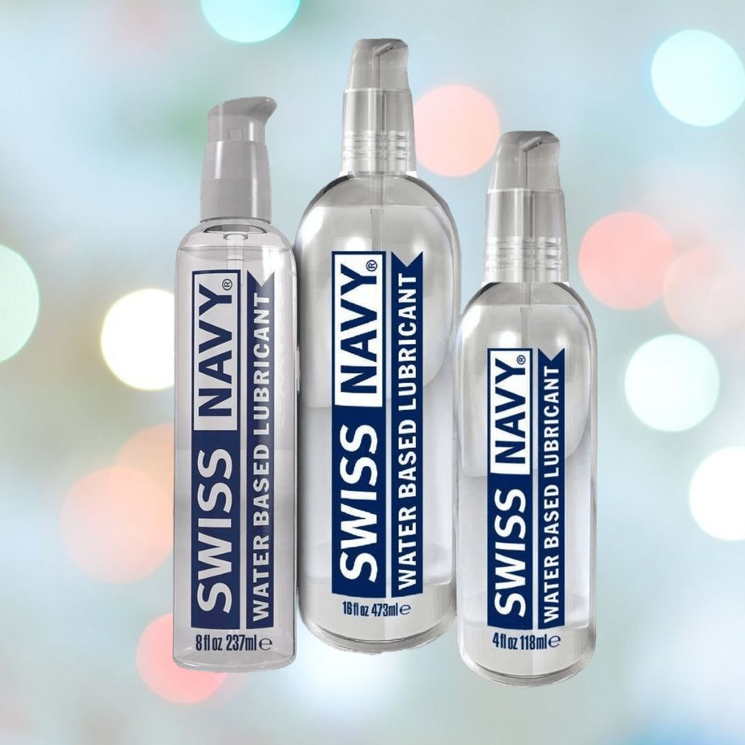 Three bottles of Swiss Navy Water-Based Lubricant are displayed against a bokeh background, showcasing their leak-proof design. The 8 oz (237 ml), 16 oz (473 ml), and 4 oz (118 ml) bottles feature a convenient pump dispenser and sport a blue and white label under the Swiss Navy brand, making them an ideal toy-friendly lube option.