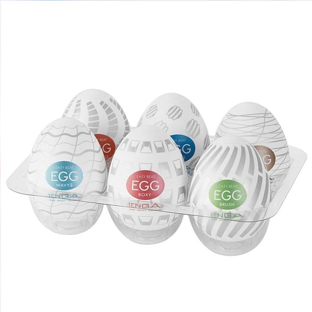 The TENGA Egg Variety Pack - Standard Penis Strokers (6 Pack) by Tenga features six white, egg-shaped sleeves, each with a colorful label and unique pattern, displayed in a clear tray.