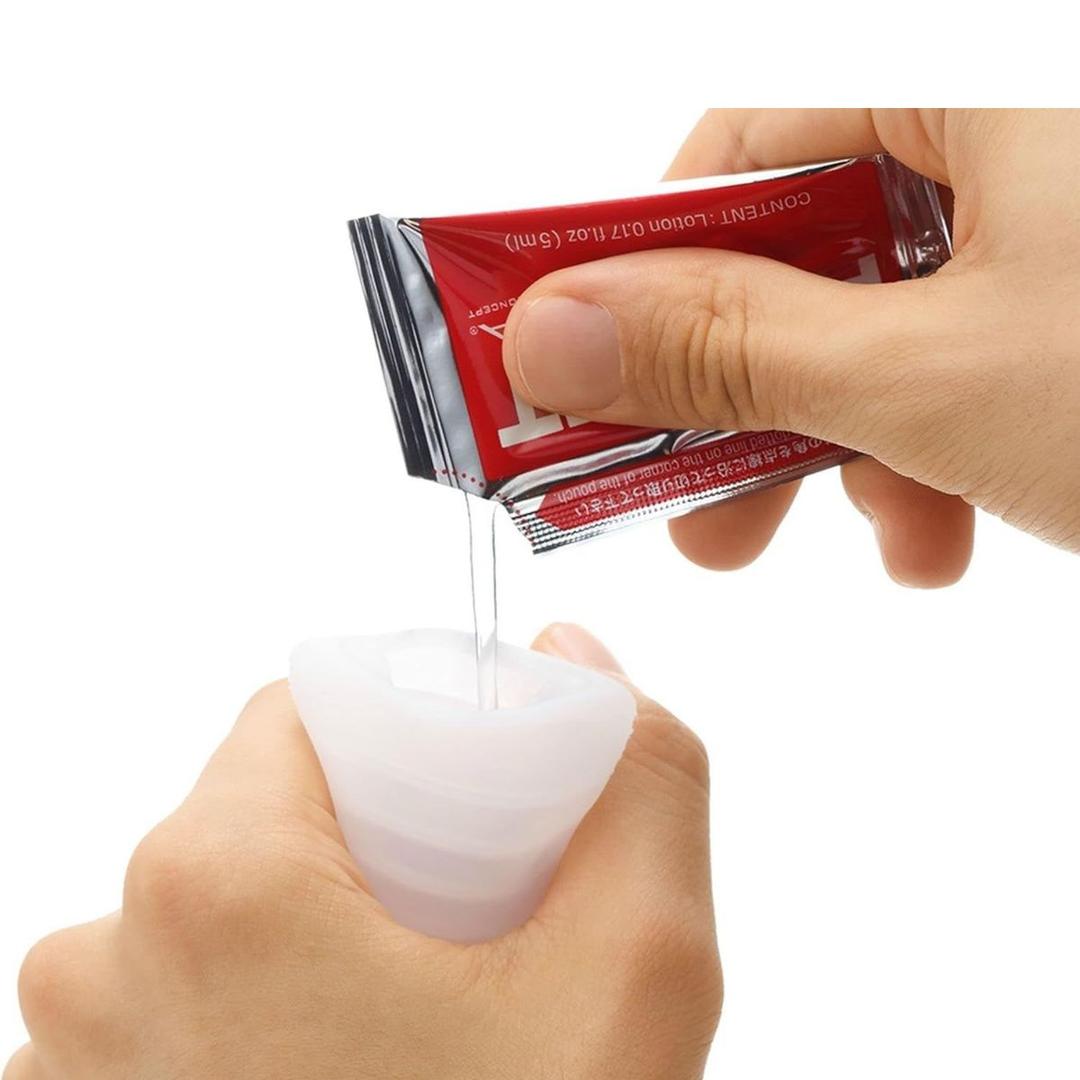 A person squeezes clear gel from a small red and silver TENGA Pocket Click Ball Disposable Textured Male Masturbator by Tenga into a white silicone container, highlighting this pocket-sized pleasure item made with super-stretchy elastomer.