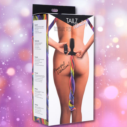 A woman holds the black Tailz Vibrating Rainbow Tail Anal Plug – with Remote-Control, featuring a long rainbow ponytail. The pink sparkly box shows the Tailz brand, perfect for pony play enthusiasts. 1080