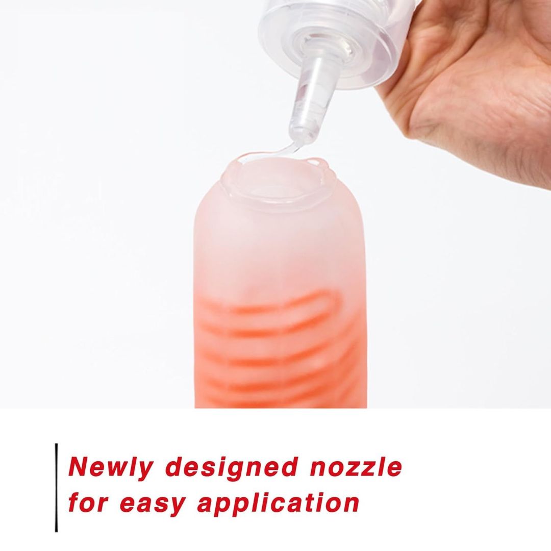 A hand holds a bottle of TENGA Hole Lotion Light Lubricant, featuring a clear nozzle that dispenses the lubricant into a red container. The text reads, "Newly designed nozzle for easy application." Ideal for use with Tenga toys.