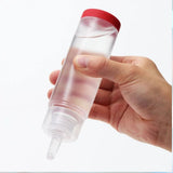 A hand holds a clear bottle of TENGA Hole Lotion "Real" Lubricant, featuring a red cap and applicator tip. The bottle, containing 5.75oz of water-based lubricant, is tilted slightly downward against a plain white background, perfect for use with TENGA toys or as a standalone product.