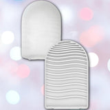 Two white silicone brush cleaning mats—one smooth, one with wave-like texture—are set against a pastel background. Their unique design echoes the travel-friendly appeal of the Tenga Pocket Wave, a disposable, smooth male masturbation sleeve by Tenga.
