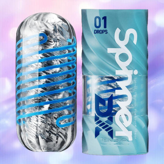 A transparent cylindrical Tenga Spinner DX 01 Drops by Tenga with a blue spiral is displayed beside its blue "Tenga Spinner DX 01 Drops" packaging, set against a soft, blurred pink, blue, and purple gradient. 1080