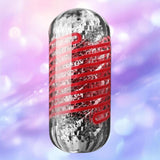 The Tenga Spinner DX 03 Steps by Tenga is a metallic, cylindrical male masturbator featuring a textured, reflective surface with red wavy lines, shown against a soft-focus purple and pink bokeh background.
