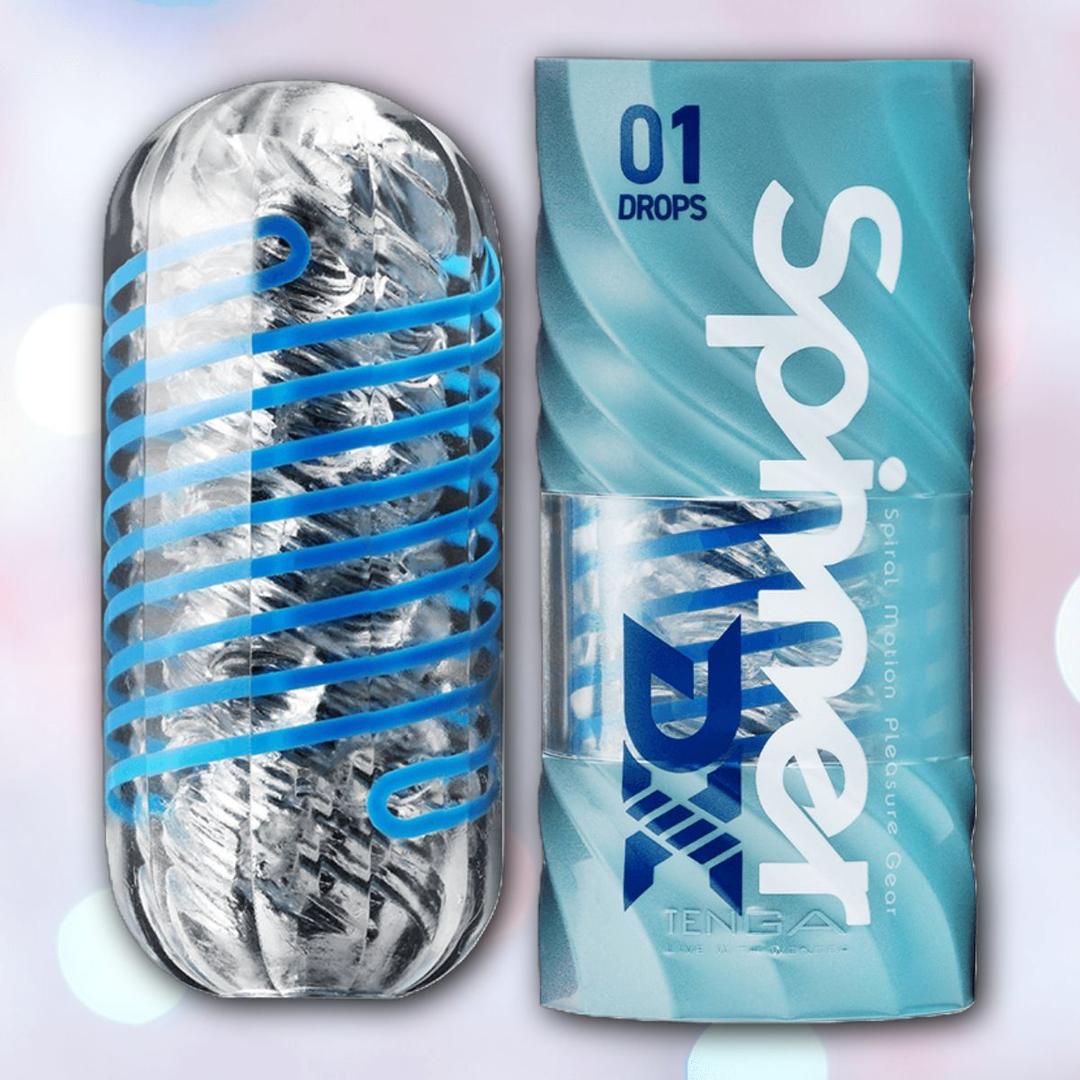 The Tenga Spinner DX 01 Drops is a clear, textured cylindrical reusable stroker with a blue spiral inside for spinning sensations, shown next to its blue and white Tenga packaging labeled "Spinner Motion Pleasure Gear.