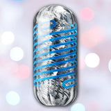A metallic capsule, the Tenga Spinner DX 01 Drops: Reusable Stroker Spinning Masturbator Sleeve by Tenga, wrapped in a blue spiral line, sits against a blurred pastel background with white and pink bokeh lights, suggesting motion.