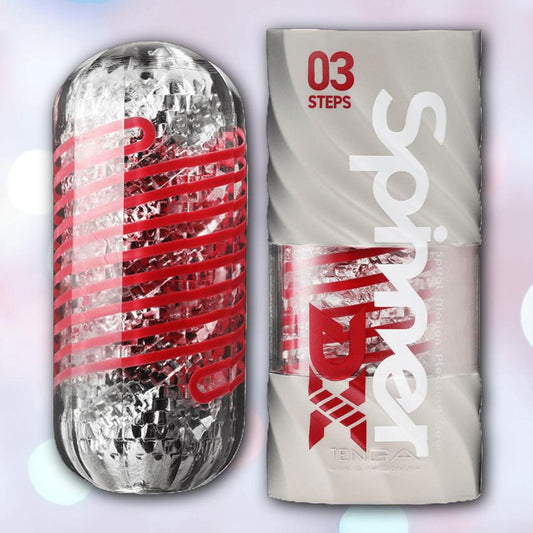 The Tenga Spinner DX 03 Steps is a reusable, transparent cylindrical stroker with a red spiral interior, shown beside its silver and white packaging, designed to deliver intense spinning stimulation for greater pleasure. 1080