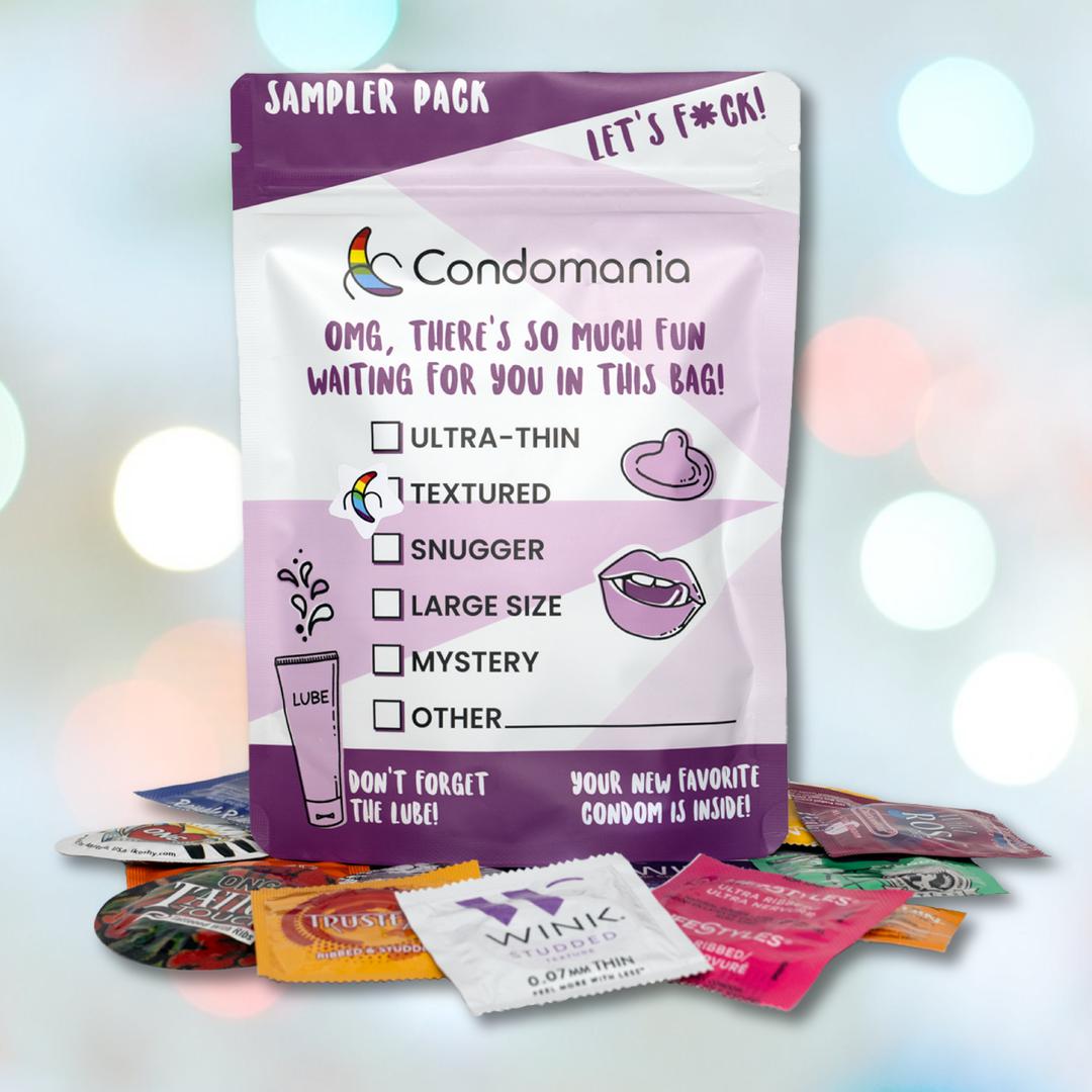 A purple and white Condomania "Textured Condom Sampler" pack lies amidst vibrant packets, featuring ribbed, studded, ultra-thin varieties, and a mystery type adorned with playful text and illustrations.