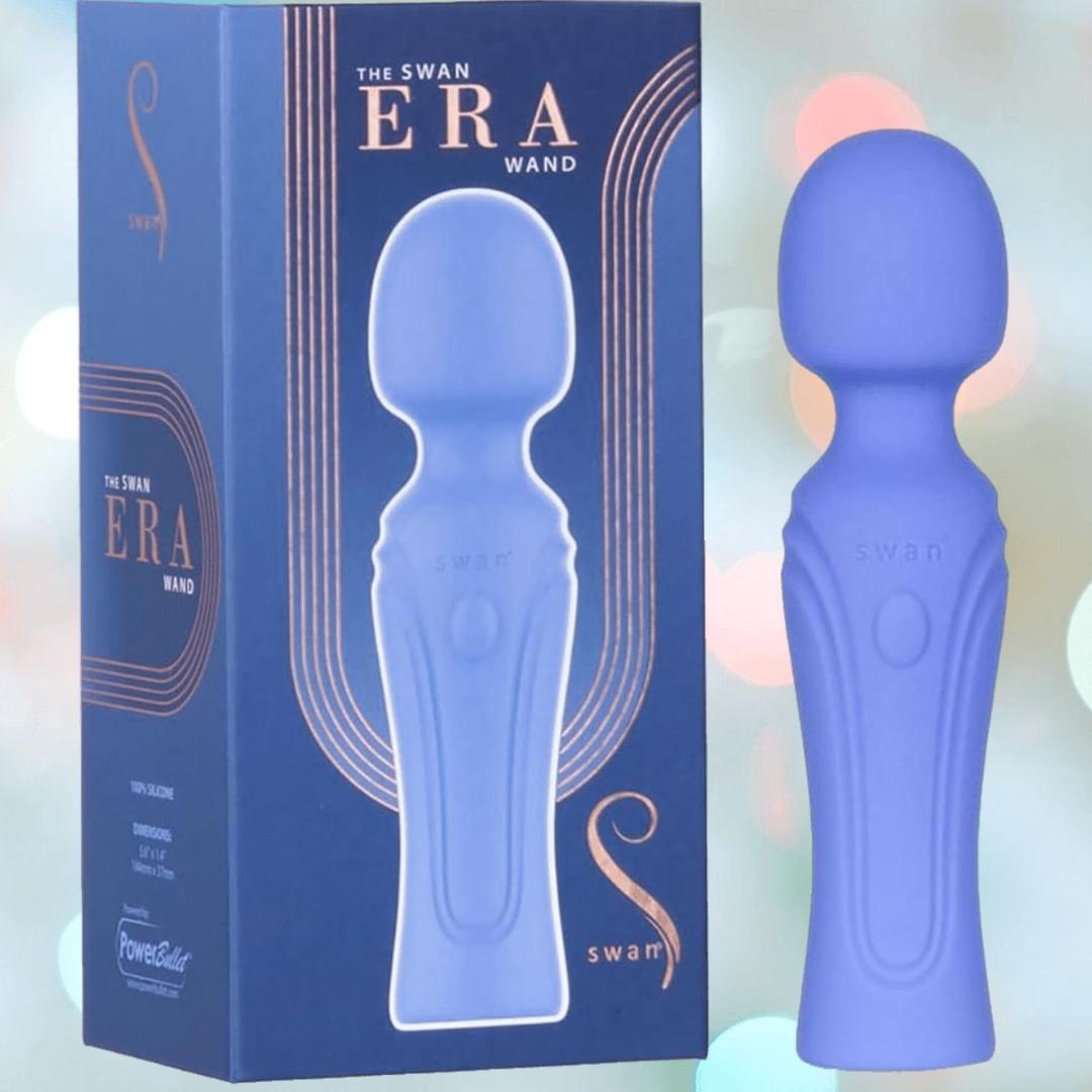 A blue BMS Swan Era Wand massager stands upright beside its matching box with gold and white branding. Featuring a PowerBullet motor for deep vibrations and precise speed control, the display sits against a softly blurred background of pastel lights.