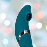 The Monarch Swan by BMS is a teal silicone G-spot vibrator featuring a curved design and silver accent band, shown against a softly blurred background with pastel bokeh lights.