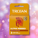 A box of Trojan Ultra Ribbed Condoms by Trojan, containing 3 ribbed condoms, is displayed against a pink and purple bokeh background.
