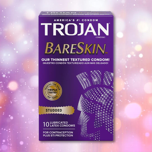 A purple box of Trojan Studded Bareskin Condoms displays gold and white text, including “Our Thinnest Textured Condom!” and “10 lubricated latex condoms,” set against a backdrop of pink and white bokeh lights. 1080
