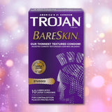 A purple box of Trojan Studded Bareskin Condoms displays gold and white text, including “Our Thinnest Textured Condom!” and “10 lubricated latex condoms,” set against a backdrop of pink and white bokeh lights.
