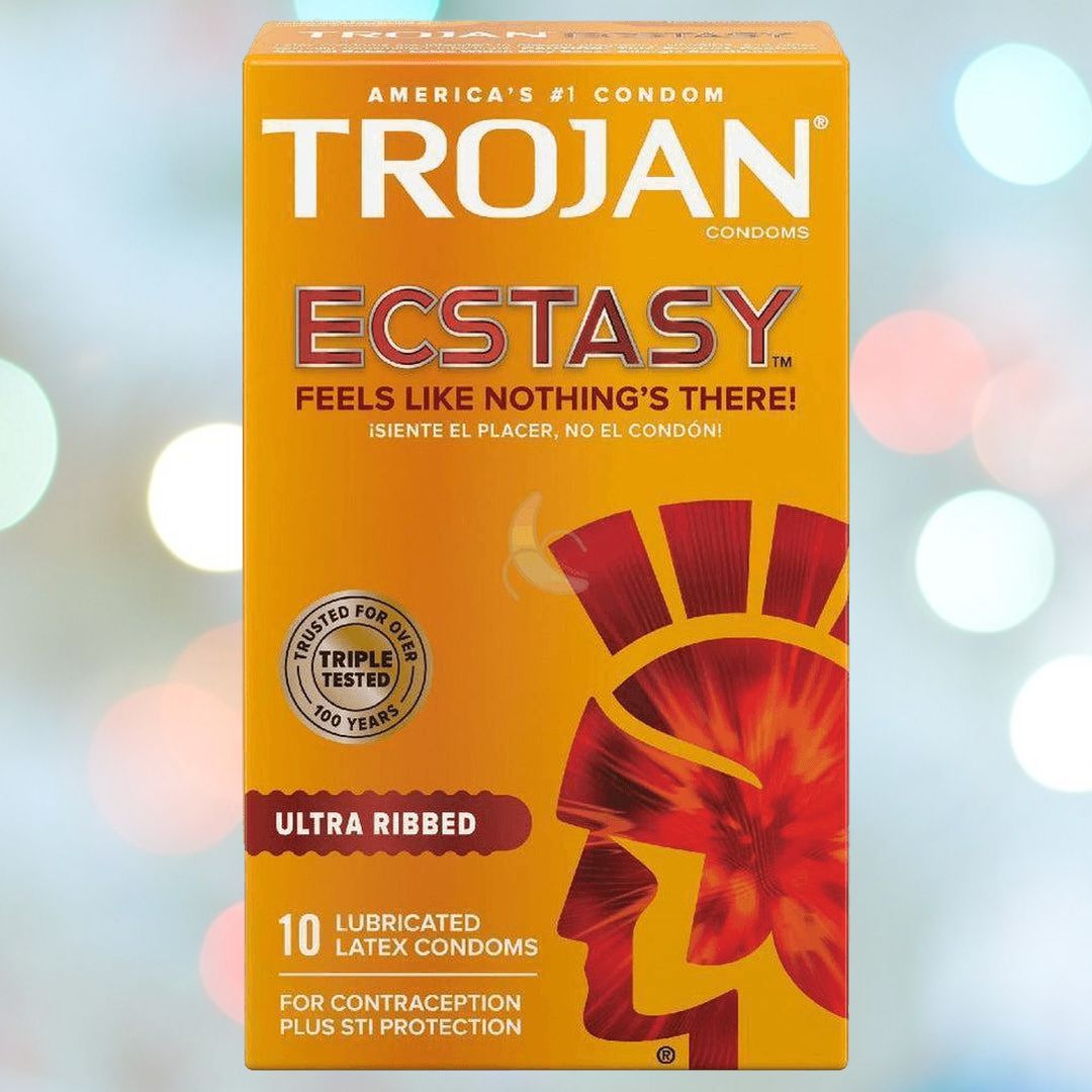 The image showcases a box of Trojan Ultra Ribbed Ecstasy Condoms by Trojan, featuring premium lubricant against a blurred background with lights. The primarily orange box, accented with red and gold, displays the phrase "Feels like nothing's there!" and contains 10 lubricated latex condoms.