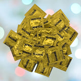 A stack of gold-colored Trojan brand Magnum Condoms is displayed against a softly blurred backdrop featuring pastel circles, emphasizing their large size and comfortable fit.