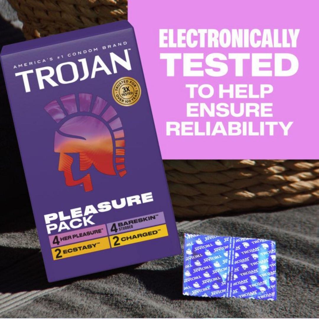 A box of Trojan Pleasure Pack Variety Condom Sampler by Trojan sits on a surface next to two opened wrappers. Text on a pink background reads: “Electronically tested to help ensure reliability in this condom sampler.”.