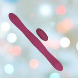 The Doc Johnson Tryst Duet Double-Ended Silicone Vibrating Dildo in Berry features a wireless remote and is shown against a soft, pastel bokeh background.