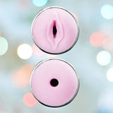 Displayed are components of the VeDO Jerk Masturbation Sleeve, featuring two pink, circular silicone parts with anatomical designs made from body-safe materials. The top part is crafted to resemble a stylized vulva, while the bottom part is designed to look like a stylized anus. The background features soft pastel colors in a blurred fashion.