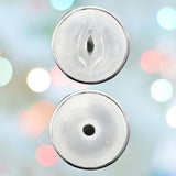 Close-up of two white circular objects with openings in the center against a soft blurred background with pastel-colored lights. The top circle, resembling a VeDO Jerk Masturbation Sleeve - Black with Clear Sleeve by VeDO, features a vertical slit, while the bottom circle has a small round hole.