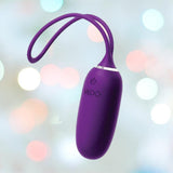 The VeDO Kiwi Bullet - Purple, a sleek personal massager made from velvety silicone, features a looped handle and side power symbol. Enhanced by soft pastel bokeh lights in the backdrop, this rechargeable vibe offers multiple vibration modes for a tailored experience.