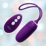 The VeDO Kiwi Bullet - Purple is a silicone, remote-controlled vibrator with a rounded hand-held remote featuring three buttons. This rechargeable device offers multiple vibration modes, with both items showcasing the "VeDO" brand against a blurred pastel light background.