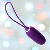 The VeDO Kiwi Bullet - Purple is an egg-shaped personal massager with a loop handle, showcased against a backdrop of blurred colorful bokeh lights.