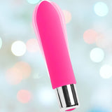 A vibrant pink VeDO Bam Mini Rechargeable Bullet Vibrator, featuring a sleek metallic silver base, set against a softly blurred backdrop of white, pink, and blue lights.