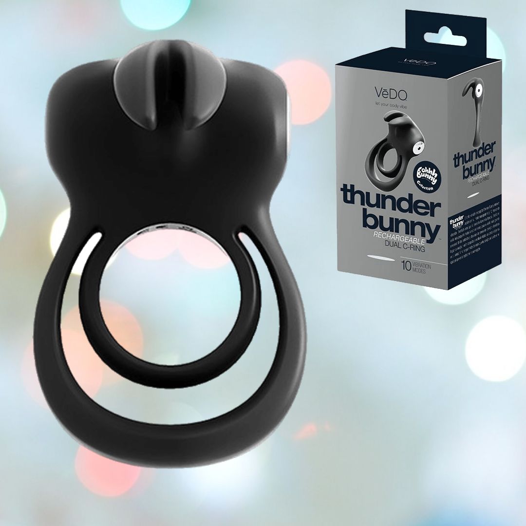 The VeDO Thunder Bunny Dual Cock Ring - Black Pearl is prominently displayed next to its stylish packaging, offering the promise of intense vibrations. In the backdrop, gentle, colorful bokeh lights heighten its appeal.