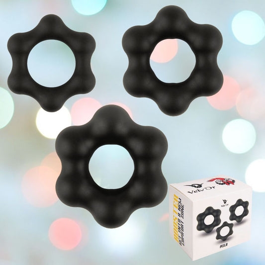 Three black, circular cock rings with a wavy texture float against a blurred background of pastel colors. A box labeled "Velv'Or" displays an image of the silicone rings and the name "Rooster Milo," reminiscent of crafting the perfect balance akin to dawn's first light. 1080