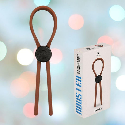 The Velv'Or Rooster Ragnar Adjustable Lasso String Cock Ring in brown is displayed with its packaging, featuring an image of the product. The background is softly blurred with pastel lights. 1080