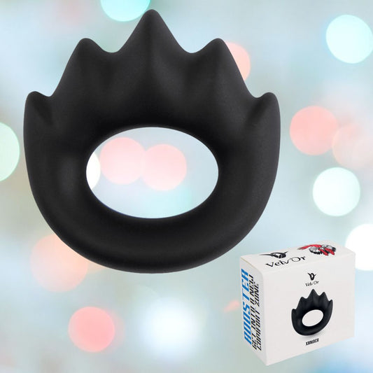 A black Velv'Or Rooster Xander Spiky Soft Silicone Cock Ring, featuring a smooth texture with spikes, is showcased against a blurred, colorful background. Beneath the ring sits a box displaying an image of the ROOSTER XANDER and its Velv'Or branding, emphasizing the packaging and robust erection benefits. 1080