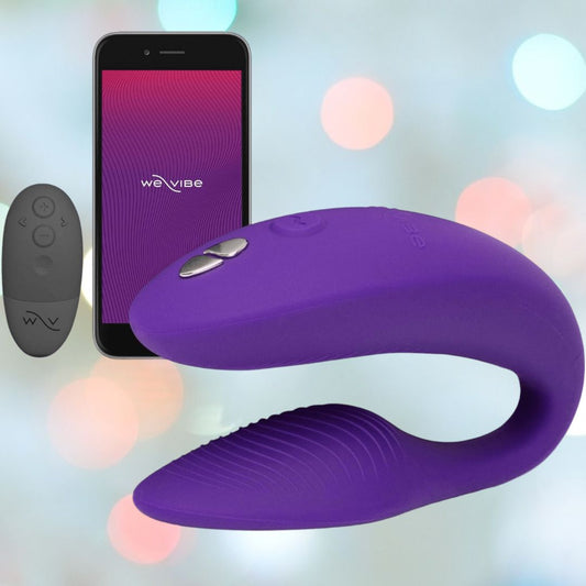 Introducing the We-Vibe Sync 2 Couples Vibrator with App in Purple, a device crafted by We-Vibe for shared pleasure. It boasts a curved design with an adjustable fit, accompanied by a remote control and app interface visible on a smartphone screen. The ambiance is set with shimmering blurred multicolored lights in the background, enhancing the enticing mood. 1080