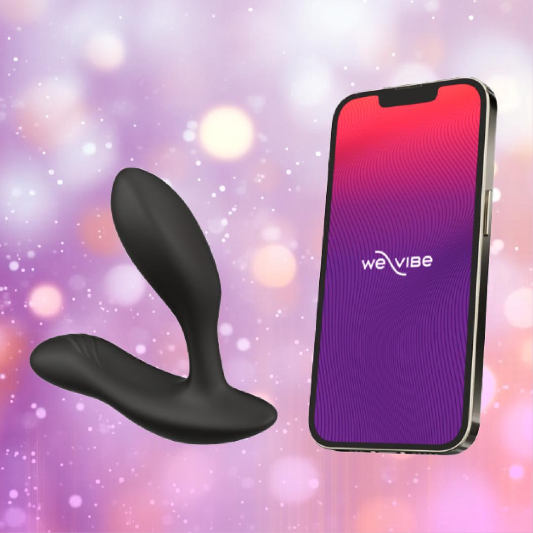 The We-Vibe Vector+ Vibrating Prostate Massager in Charcoal Black is shown beside a smartphone with the We-Vibe app, set against a purple and pink bokeh background.