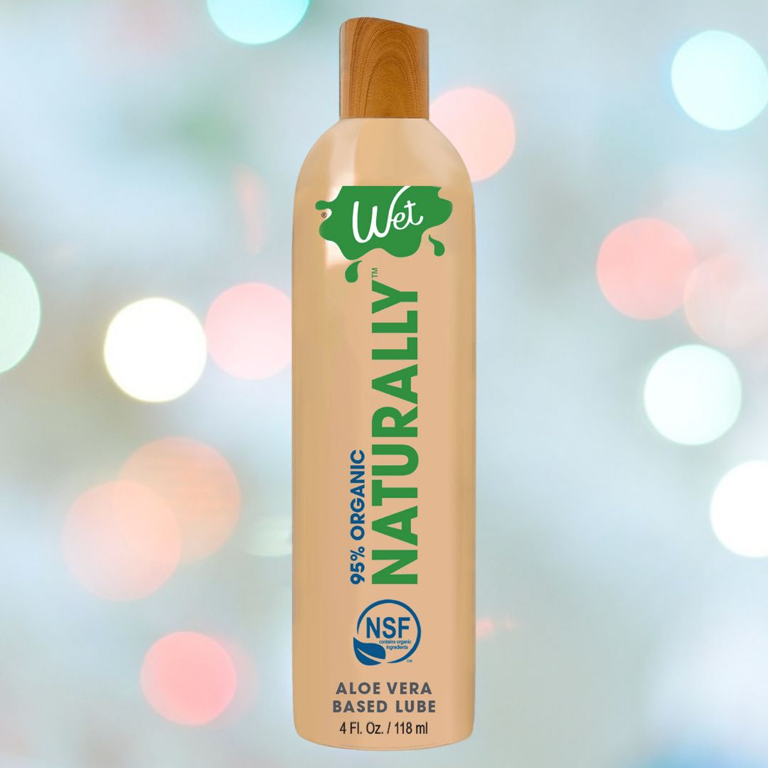 A bottle of Wet Naturally - 95% Organic Aloe Based Lubricant by Wet, containing aloe vera and NSF certification, is presented with a wooden cap against a soft-focus, bokeh background.