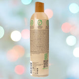 The bottle of Wet Naturally features a wooden cap with text and symbols indicating it is an environmentally friendly, vegan lubricant made with 95% organic aloe. The blurred background of colorful bokeh lights adds a festive atmosphere.