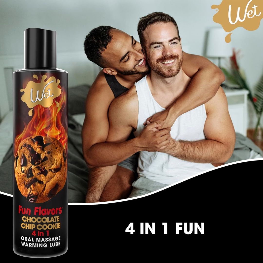 Two joyful men hugging on a bed beside a bottle of Wet Desserts 'Chocolate Chip Cookie' Warming Lubricant 🍪. The image text states, "4 in 1 Fun: edible and warming.