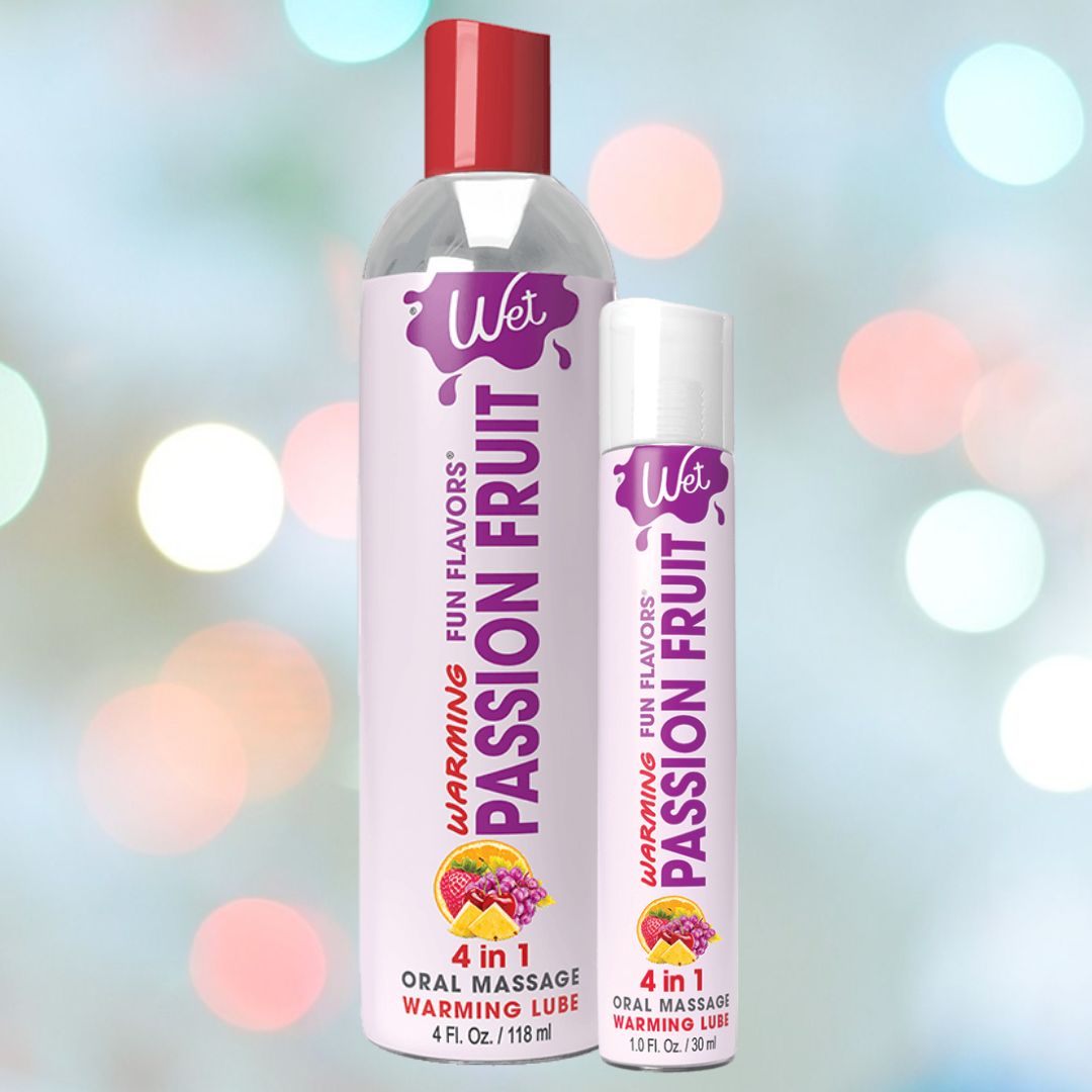 Two bottles of Wet "Passion Punch" Warming Lubricant 🍊 are displayed against a soft, blurred background with circular light spots. The larger bottle is 4 oz and the smaller one is 1 oz. Both feature a purple logo and fruit graphics, highlighting their latex-friendly formula.