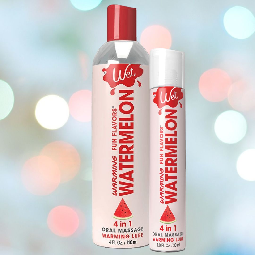 Two containers of "Wet Fun Flavors Watermelon Warming 4-in-1 Lubricant" are on display—one larger bottle with a red cap and a smaller tube, set against a backdrop of colorful lights. The labels emphasize the warming feature and the vibrant watermelon flavor, making it ideal for a flavored massage lotion experience.