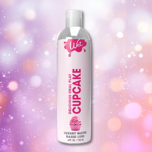 A bottle of Wet Cupcake Flavored Water Based Lube stands upright against a soft, pastel bokeh background with pink, purple, and white light circles, highlighting this luxury product by Wet. 1080