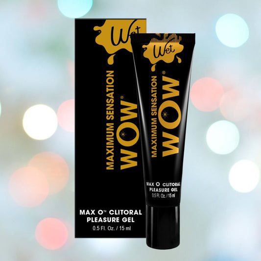 A tube of Wet WOW "Max O" Clitoral Arousal Gel, approved by Condomaniac, is set against soft pastel lights. The black packaging with bold yellow text highlights its vasodilators designed to enhance pleasure. 1080