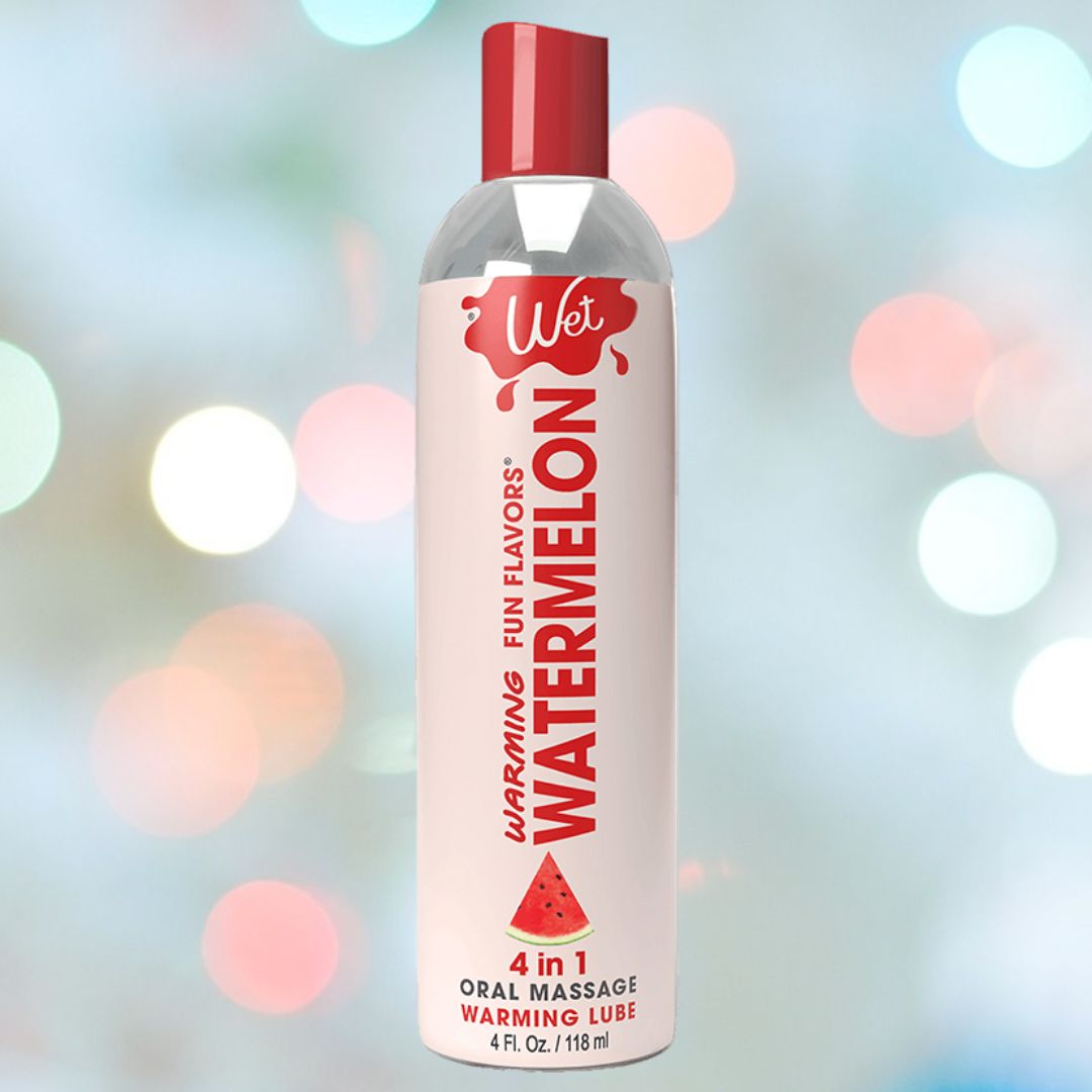 A bottle of Wet Fun Flavors Watermelon Warming 4-in-1 Lubricant 🍉, showcasing its "4-in-1" features and "Fun Flavors," rests against a backdrop of colorful, blurred lights, offering an exciting massage experience.