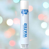 A 1.0 fl oz (30 ml) bottle of Wet Water-Based Lubricant by the brand Wet is elegantly displayed against a soft-focus background adorned with pastel circles resembling light bokeh effects, assuring users of stain-free and versatile pleasure.