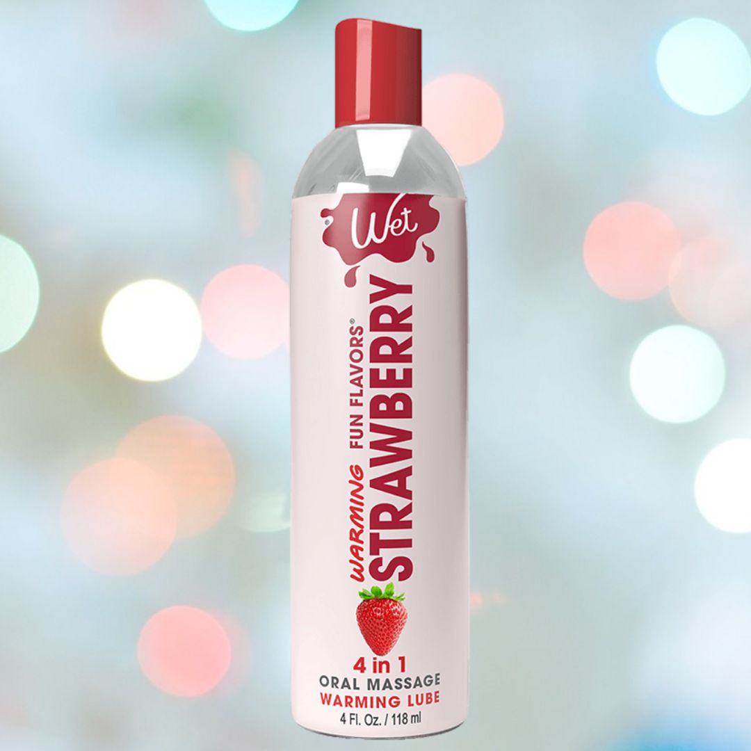 A bottle of Wet "Sexy Strawberry" Warming Lubricant 🍓, featuring a red cap and labeled "4 in 1." The water-soluble formula provides an inviting touch against a softly shimmering background with multicolored bokeh lights.