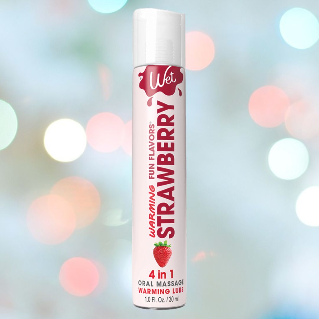 A tube of Wet "Sexy Strawberry" Warming Lubricant 🍓 is set against a blurred background with vibrant bokeh lights. This sugar-free product by Wet is designed to enhance your sensory experience.