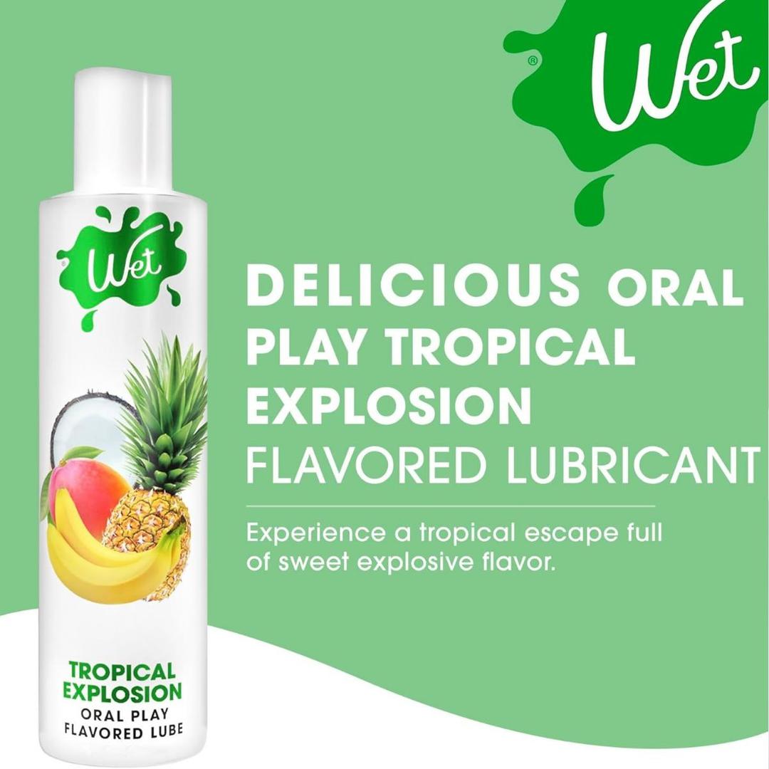 A bottle of Wet "Tropical Explosion" Warming Lubricant 🍍 is shown with mango, banana, and pineapple, described as a delicious tropical escape from Wet for sweet, explosive flavor and enhanced oral play.